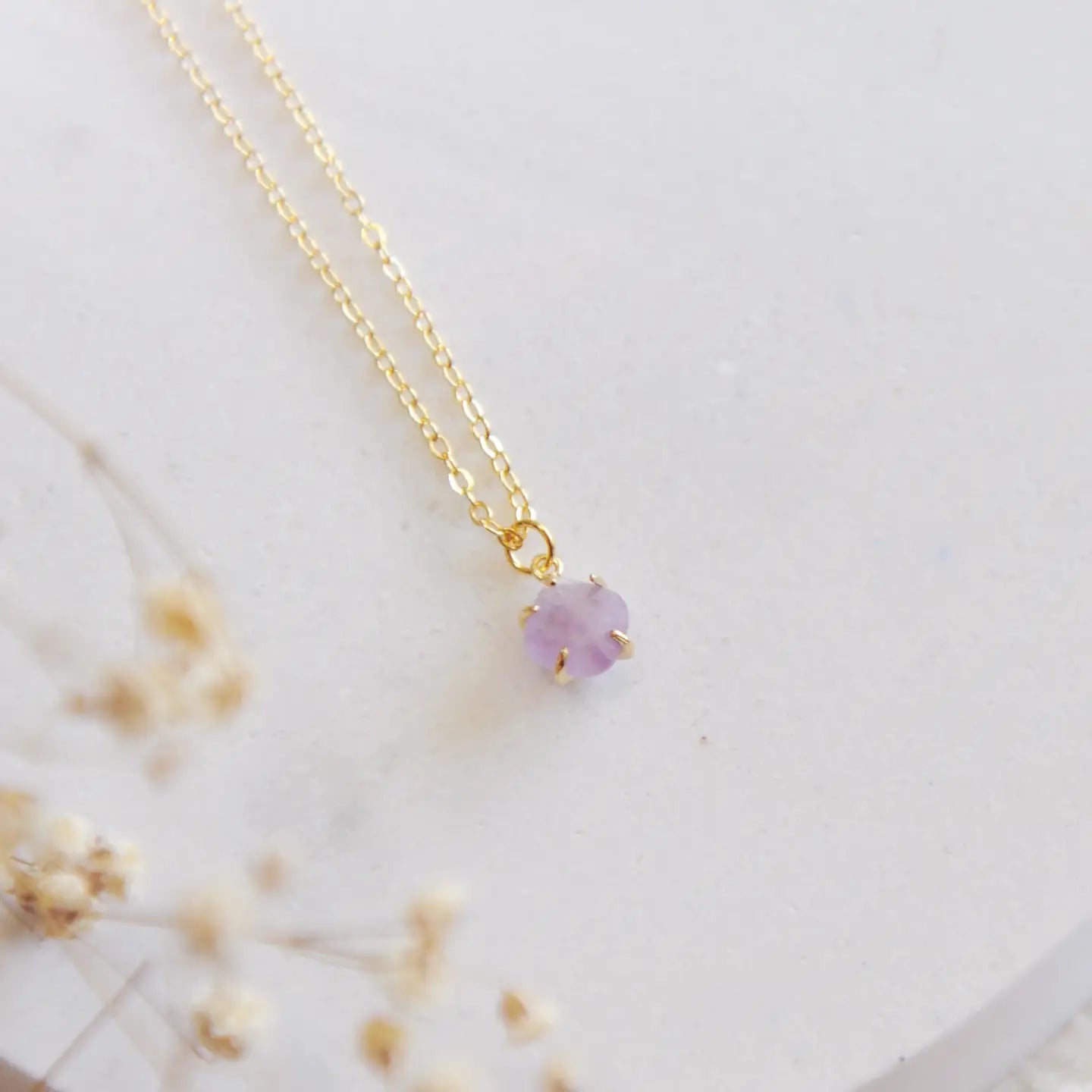 Gold necklace with a purple amethyst stone on a white stone backdrop