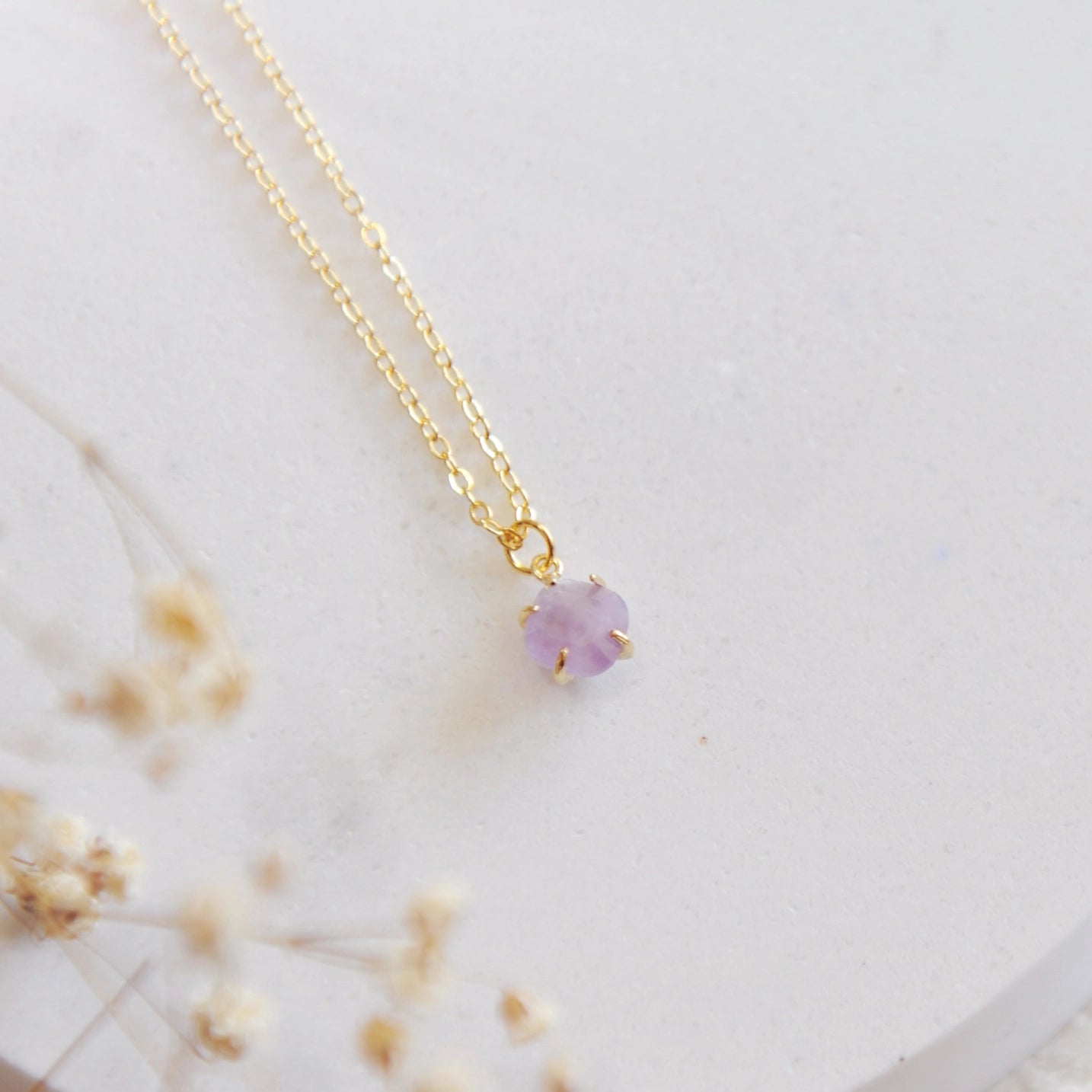 Gold necklace with a purple amethyst stone on a white stone backdrop