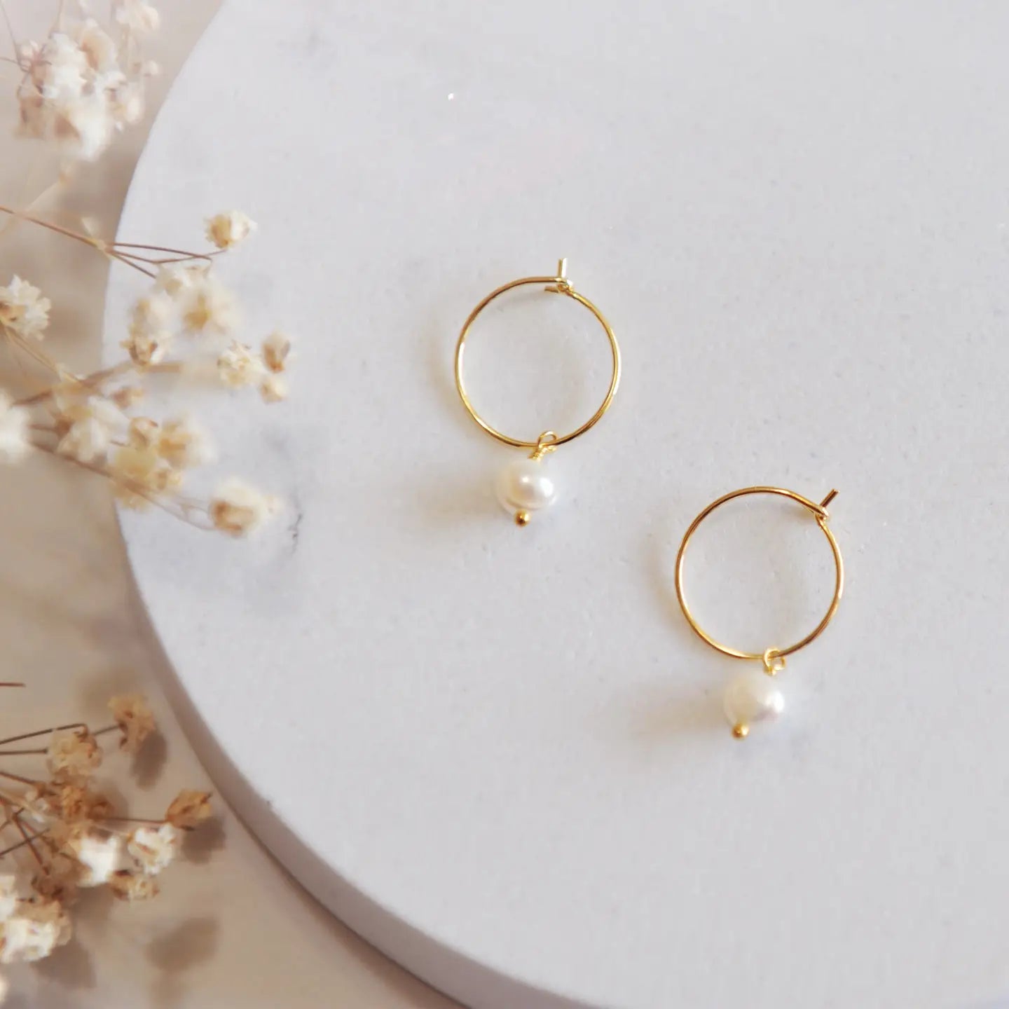 Gold hoops with a pearl on a white backdrop