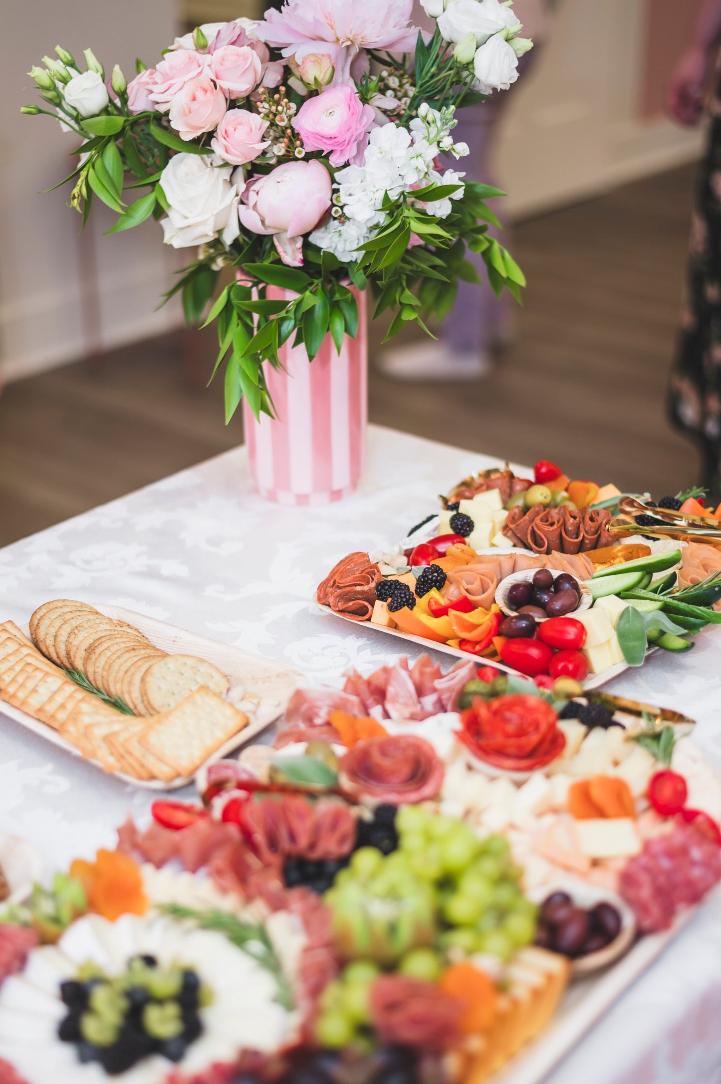 Assorted food platter with fruits, meats, and a floral arrangement on a table.