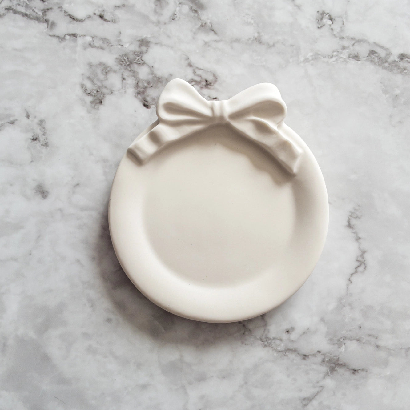 Coquette style circular ivory jewelry dish sitting on top of a marble countertop