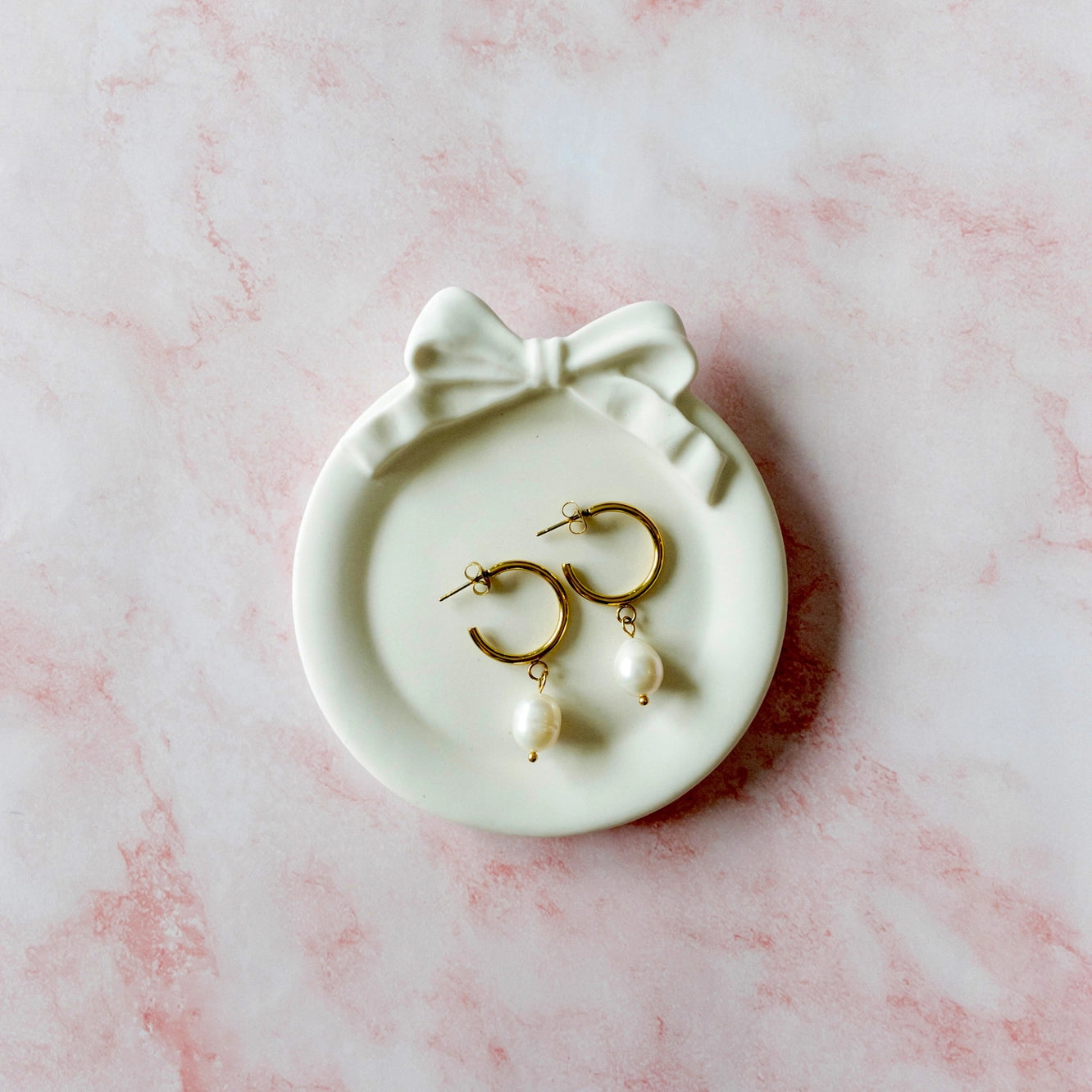 Bow Jewelry Dish, round shape featured sitting on a pink marble countertop with pearl earrings to show scale