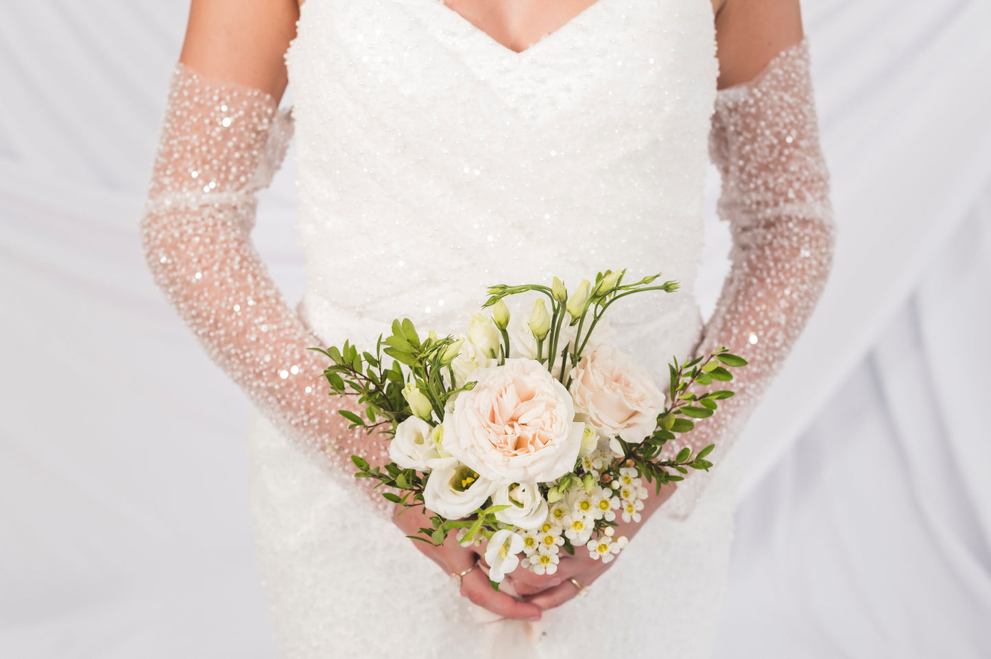 Bride holding a bouquet of flowers from Goldie Florals, with sparkly gloves on a light background