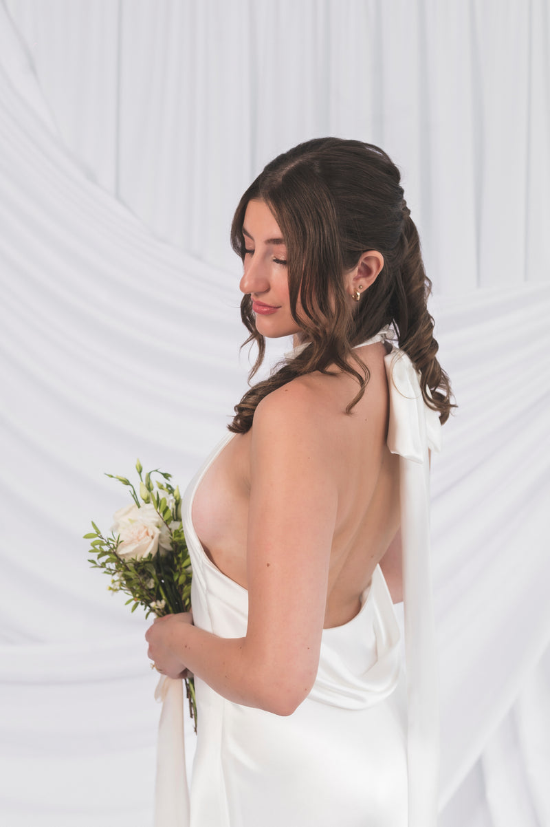 Bride showing off the low side halter wedding dress with a swooped backline and side view. Showing the optional big oversized bow at the back