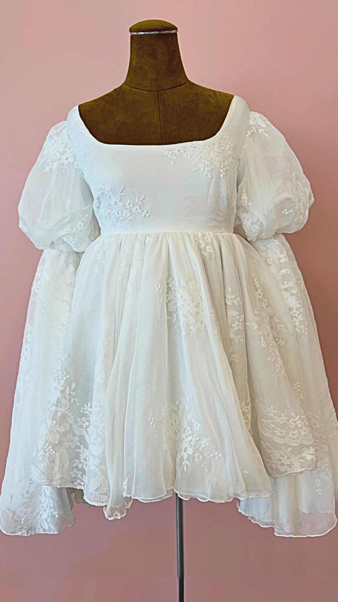White lace dress on a mannequin against a pink background