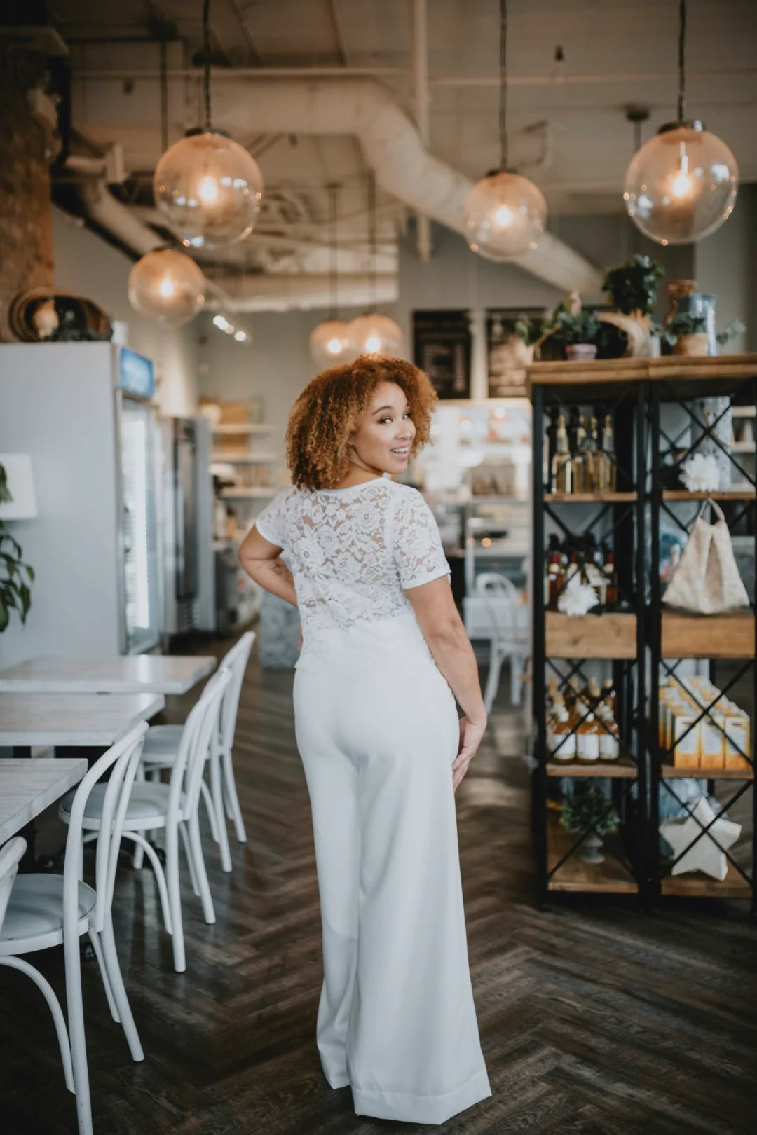 Woman in a white lace top with a jac pant standing in a modern cafe.