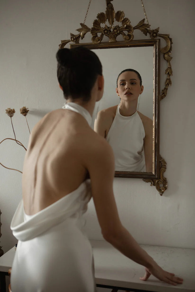 A bride looking in the mirror with a low swooped back and a very siple satin bodice