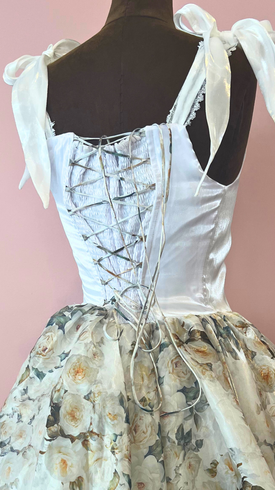 White corset-style dress with floral skirt on a mannequin against a pink background