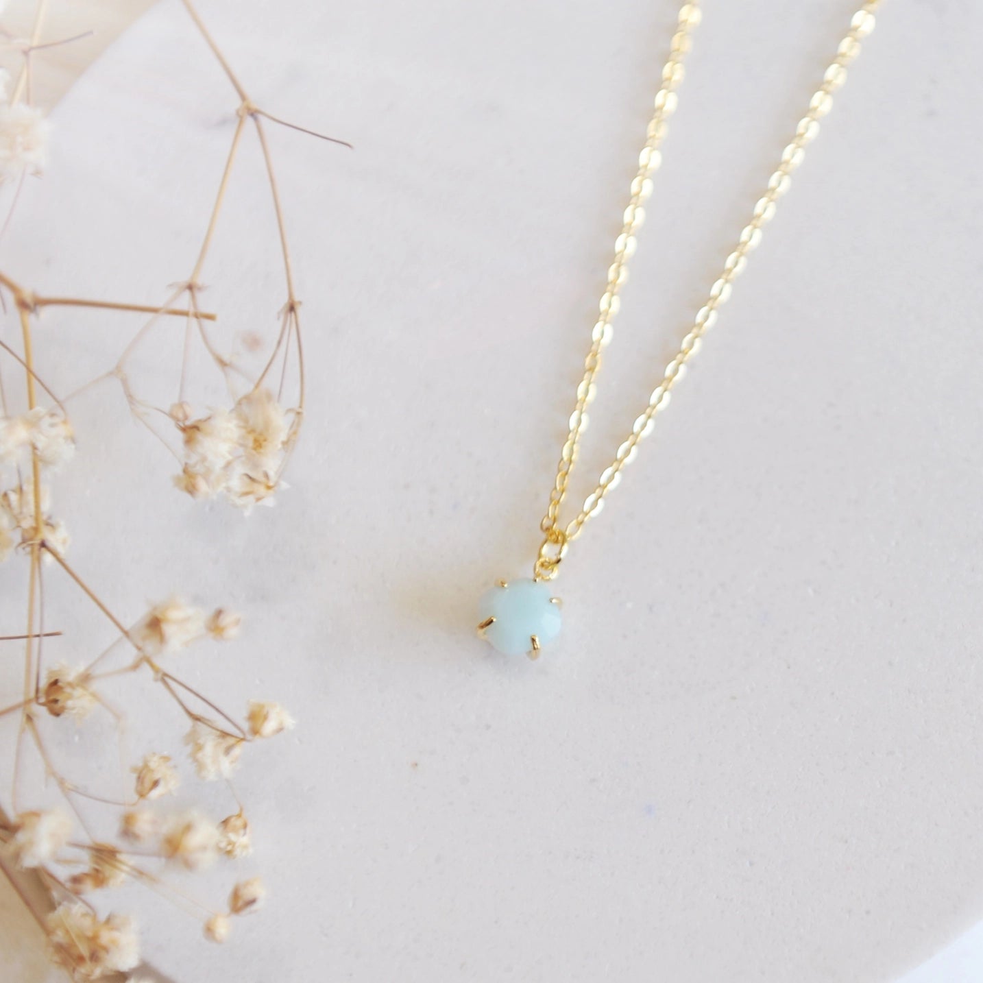 Gold necklace with a blue amazonite stone on a white stone backdrop