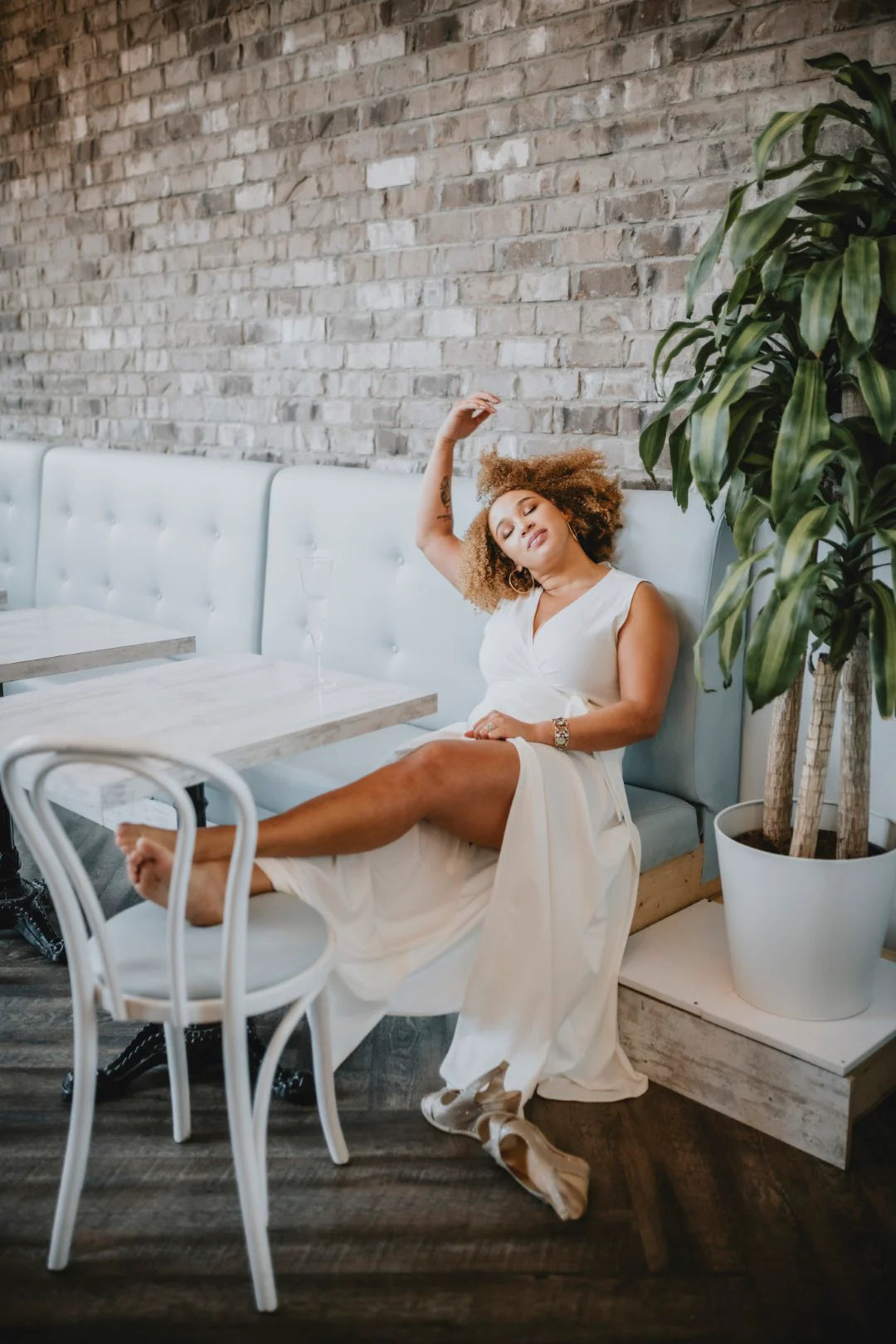 Woman in a white dress sitting on a light blue sofa with a plant and chair in the background.