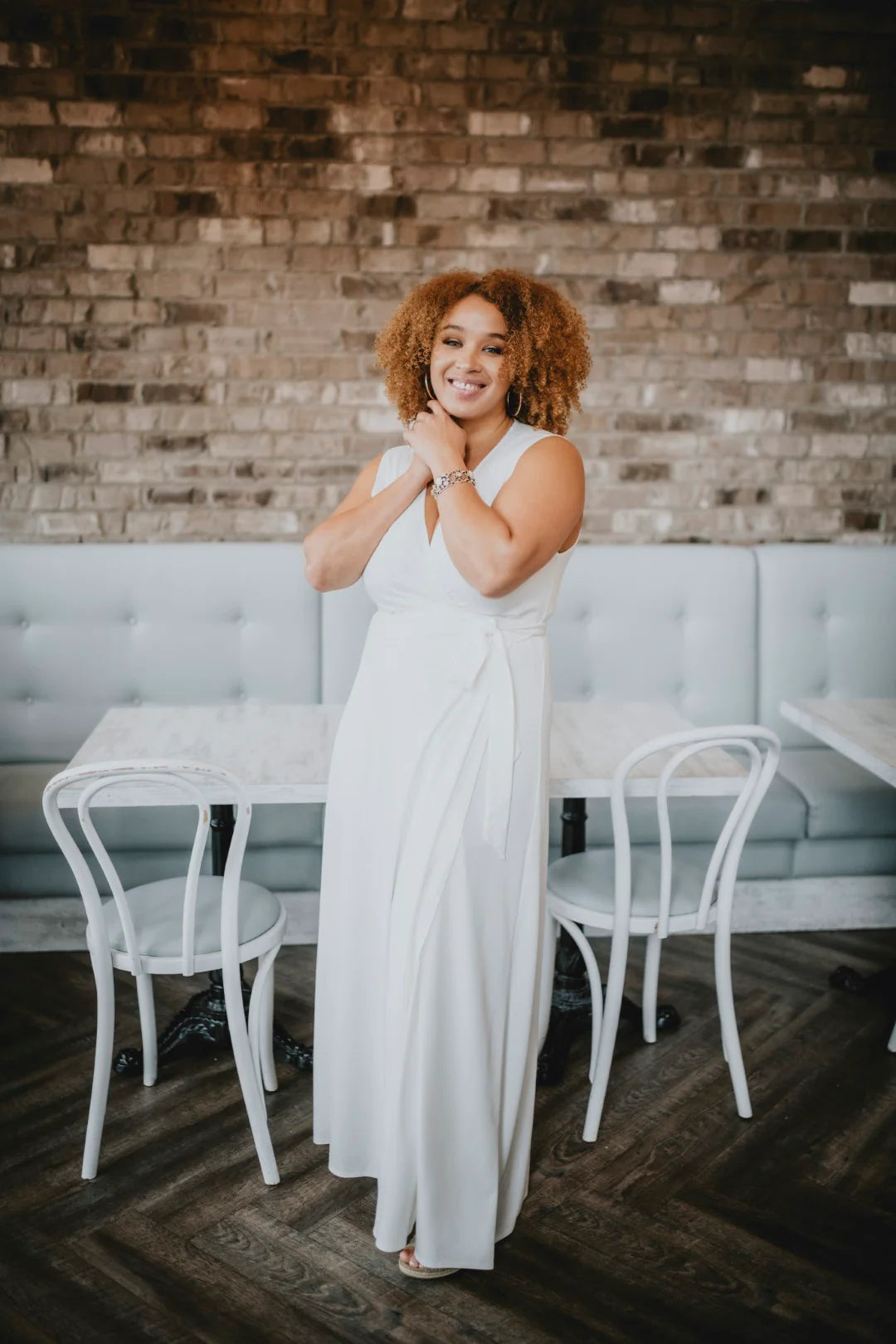 Woman in a white dress standing in a restaurant with a brick wall background