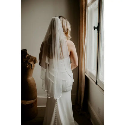 Model wearing a fingertip length satin trim veil