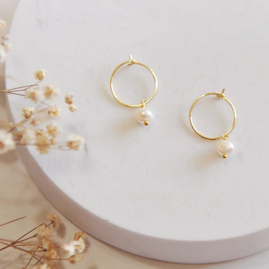 Gold hoops with a pearl on a white backdrop