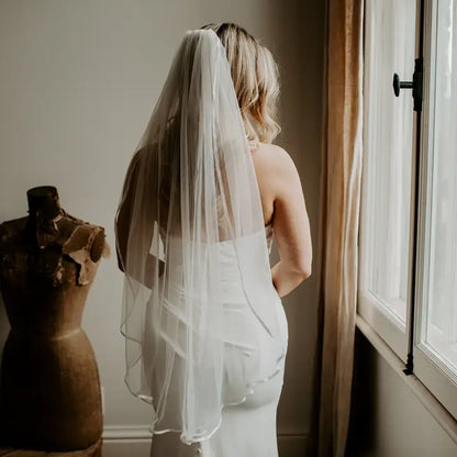 Model wearing a fingertip length satin trim veil
