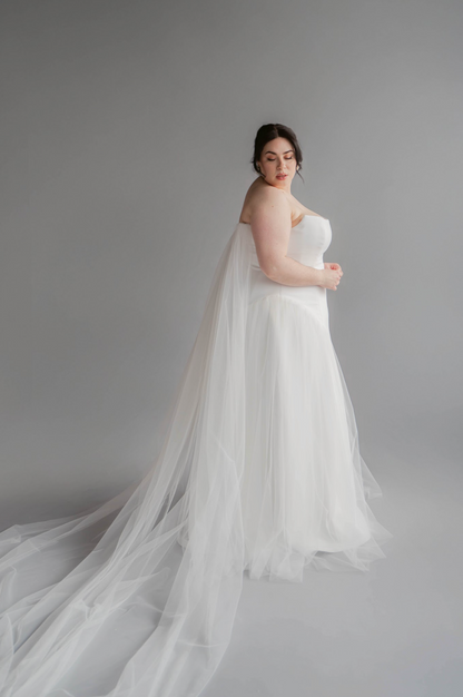 Woman in a white strapless gown with a long train against a gray background