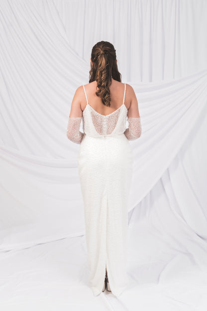 Bride showing off the back of the sparkly column shift dress with sleeves. Peakaboo sparkly back with a back slit and no train