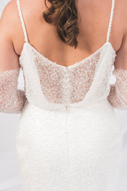 Close-up of a white beaded dress with thin straps with delicate pearl buttons unti, the waistline against a Bridal draped background