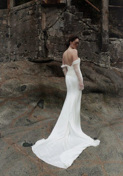 Bride in a white wedding dress, Elysian by Ouma, wfeaturing the off the shoulder soft sweatheart neckline and fitted satin silk bodice. Pearl buttons cascading down the back bodice and a modest cathedral length train. 