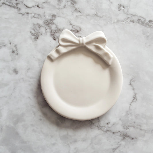 Coquette style circular ivory jewelry dish sitting on top of a marble countertop