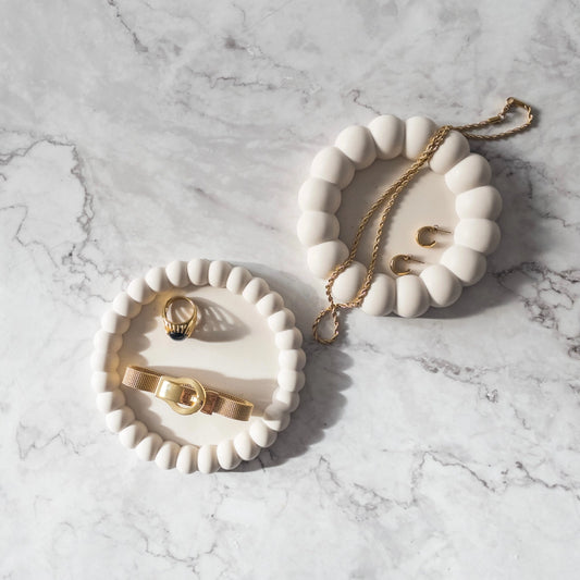 Two Ring Dishes side by side. One ring dish includes small bubbles and is holding a bracelet and ring for size. The other dish is showing the big bubble variation holding a necklace and earrings for scale. Both sit on top a marble countertop