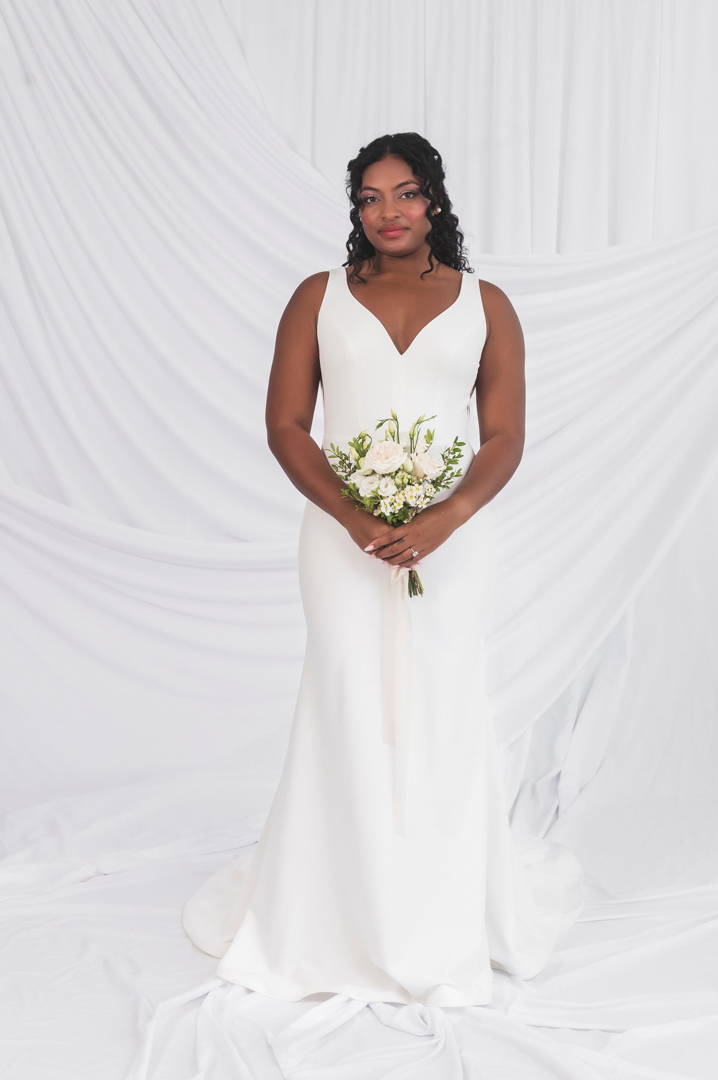 Bride wearing the v-neck clara gown in a fit and flare silhouette, matte crepe; holding a bouquet