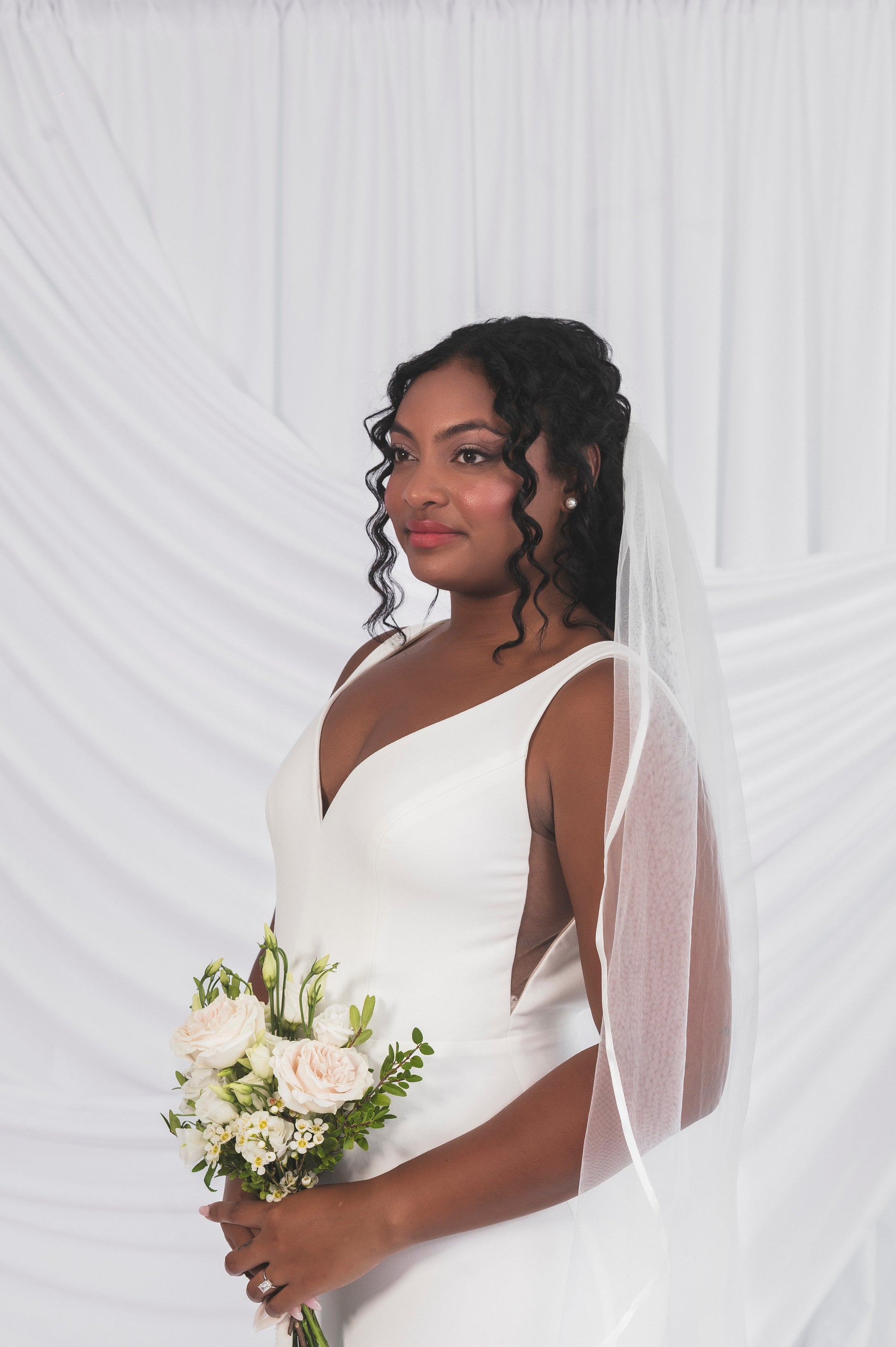 Closeup of the calara Gown, V-neckline, open sides. The Bride is wearing a simple veil with satin edges.