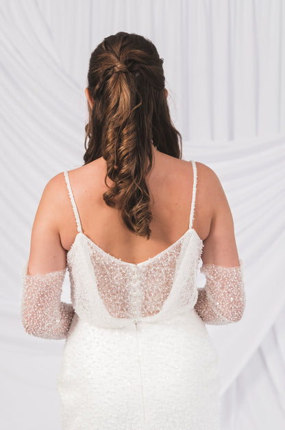 Back view of of a white beaded, Ariel/Tessa, dress with thin straps with delicate pearl buttons unti, the waistline against a Bridal draped background