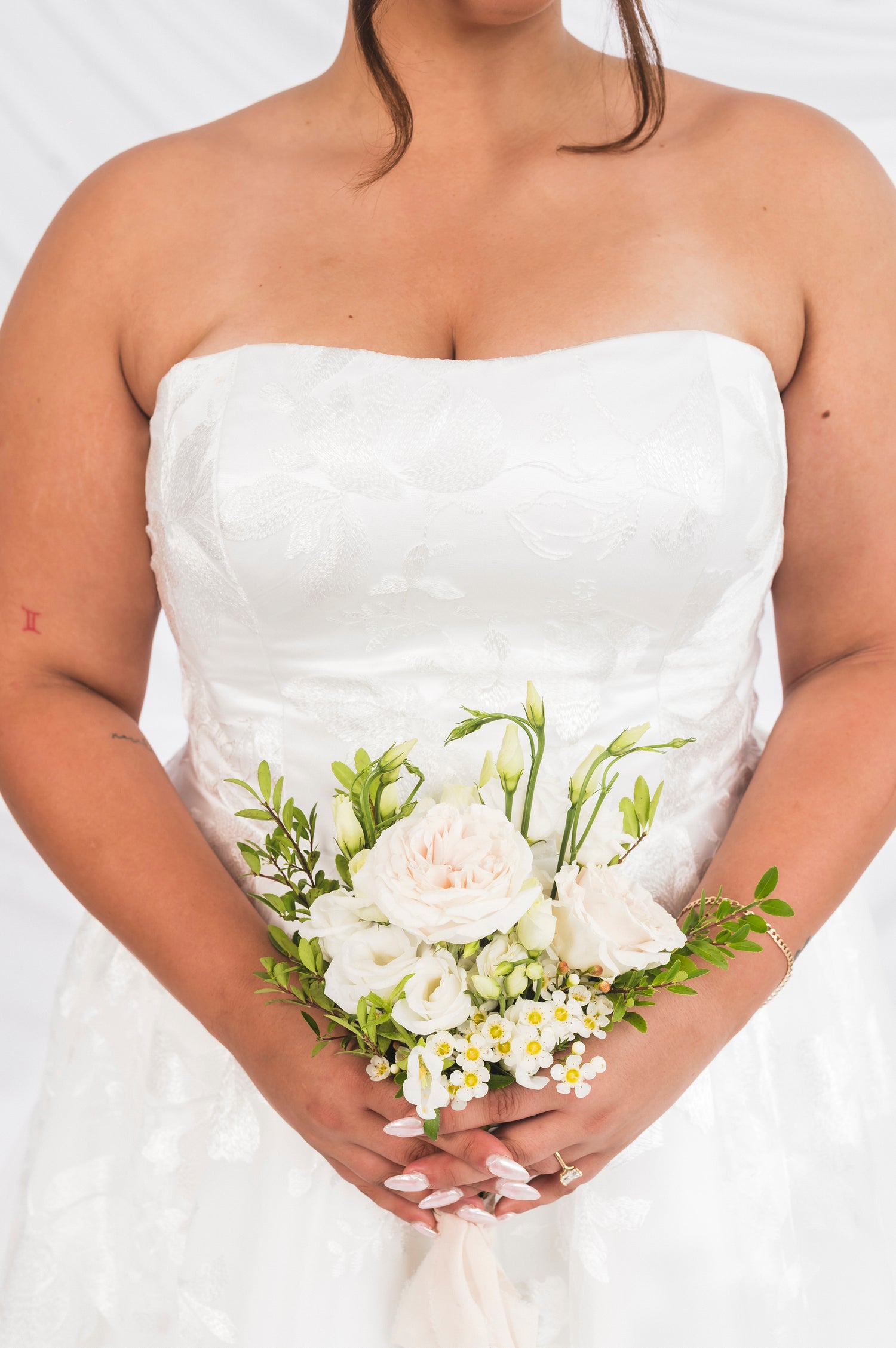 Closeup of the straight across neckline of the Juniper/Sadie, classic lace on a plus size bride in Ottawa, she is also holding a bouquet.