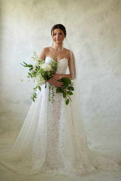 Constance is a stencil lace basque waistline gown featuring a corset bodice, deep plunge and button closure. The skirt finishes in a lace edge, showcasing the beautiful lace detailing. 