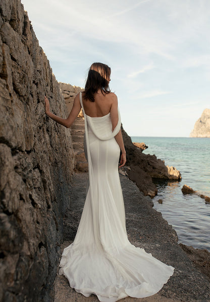 Woman in a white dress standing by a rocky coastline with water in the background