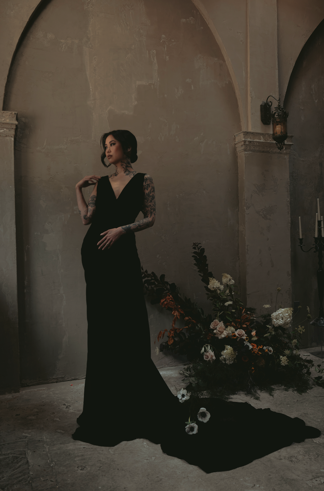 Woman in a black dress wedding standing in a dimly lit room with floral arrangements , gothic bridal ottawa