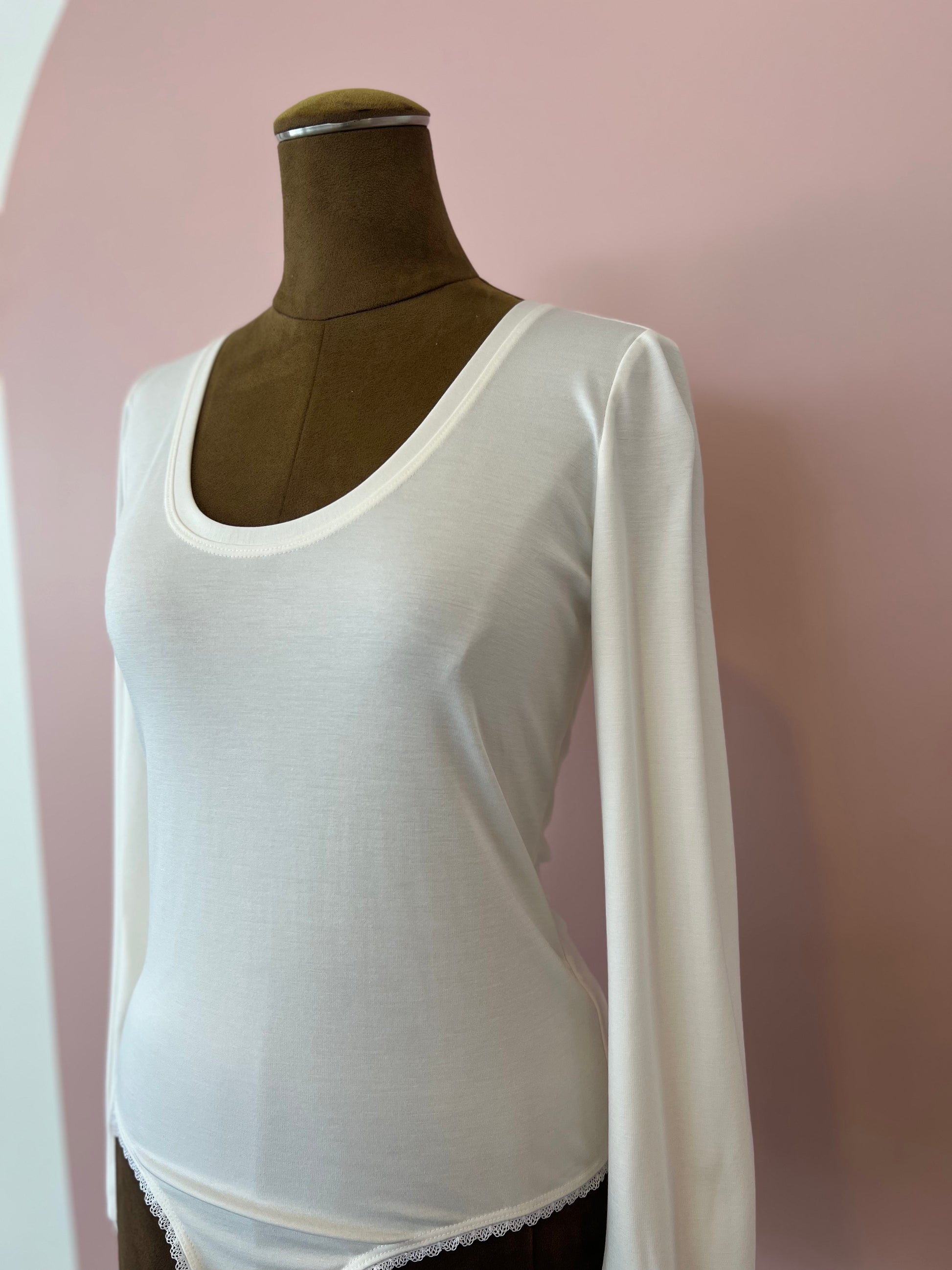 White long-sleeve top on a mannequin against a pink background