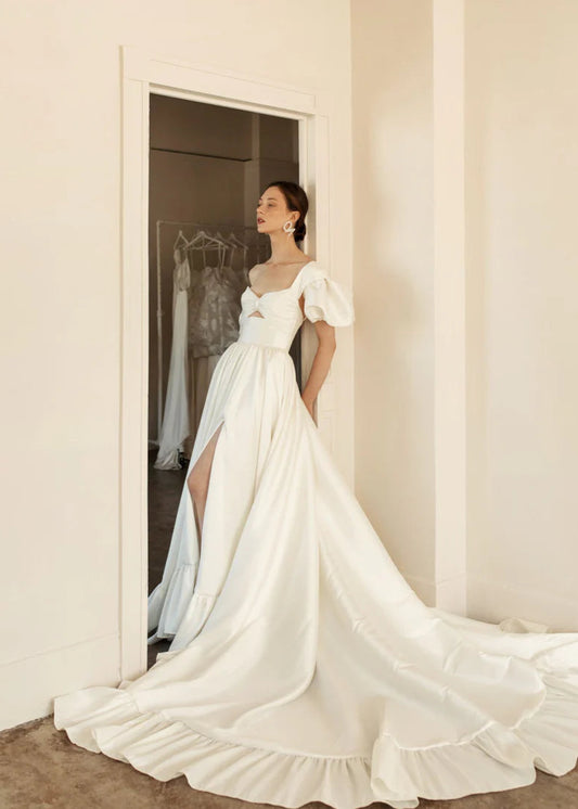 Hazel is a statement dress. Made of luxurious Mikado, this a-line piece with a peek-a-boo twisted bodice is a show stopper. A gathered skirt with a ruffled edge and a subtle leg slit create the dream gown.