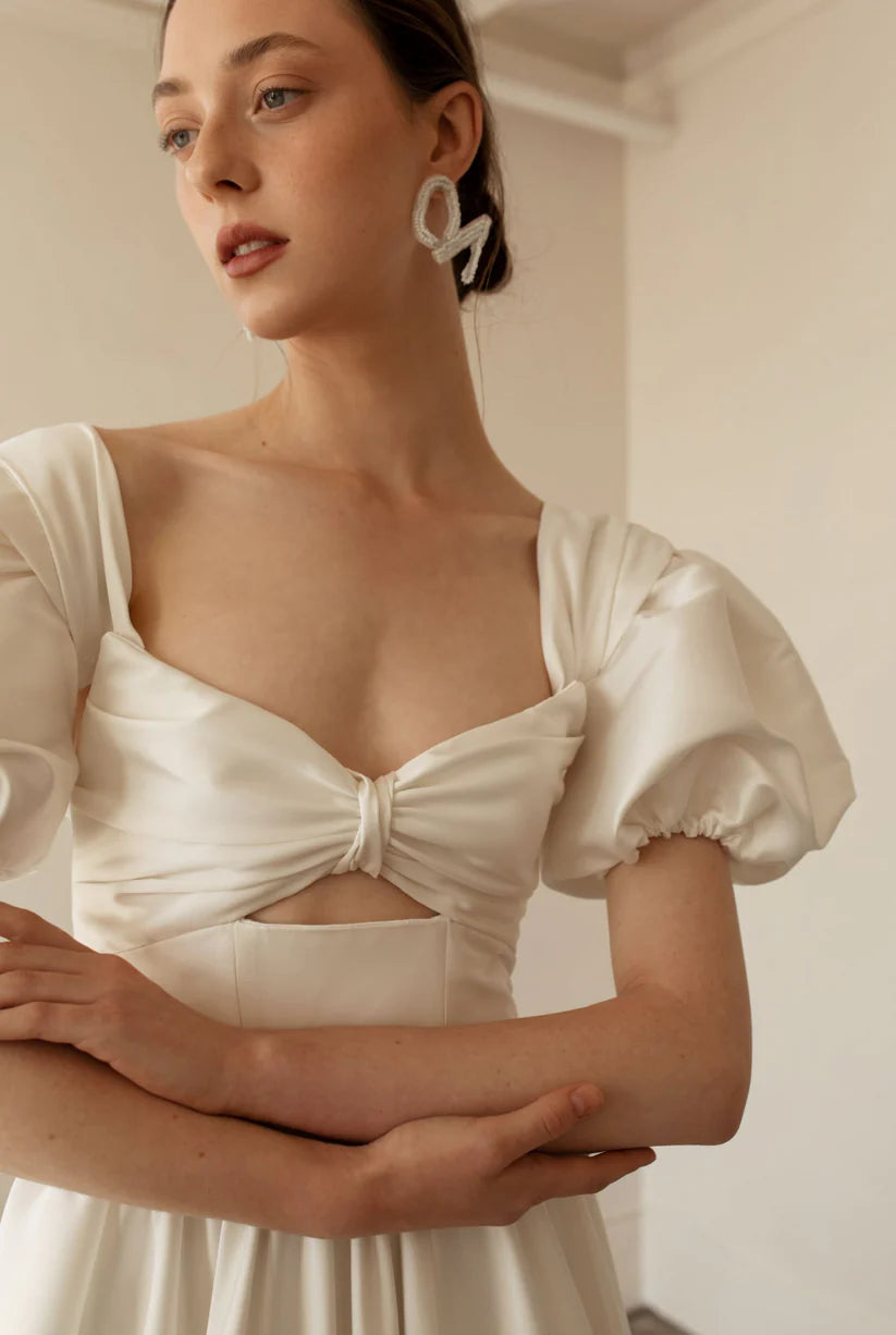 Hazel is a statement dress. Made of luxurious Mikado, this a-line piece with a peek-a-boo twisted bodice is a show stopper. A gathered skirt with a ruffled edge and a subtle leg slit create the dream gown.