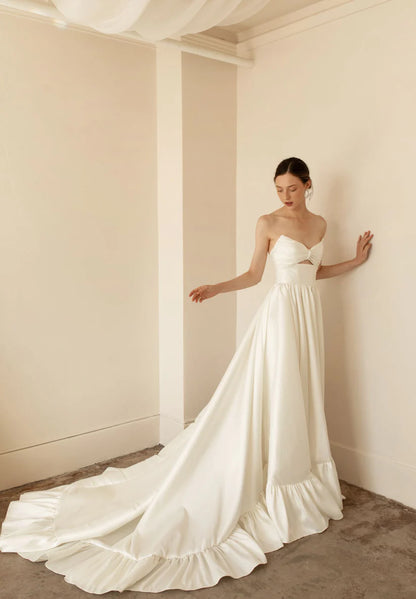 Hazel is a statement dress. Made of luxurious Mikado, this a-line piece with a peek-a-boo twisted bodice is a show stopper. A gathered skirt with a ruffled edge and a subtle leg slit create the dream gown.