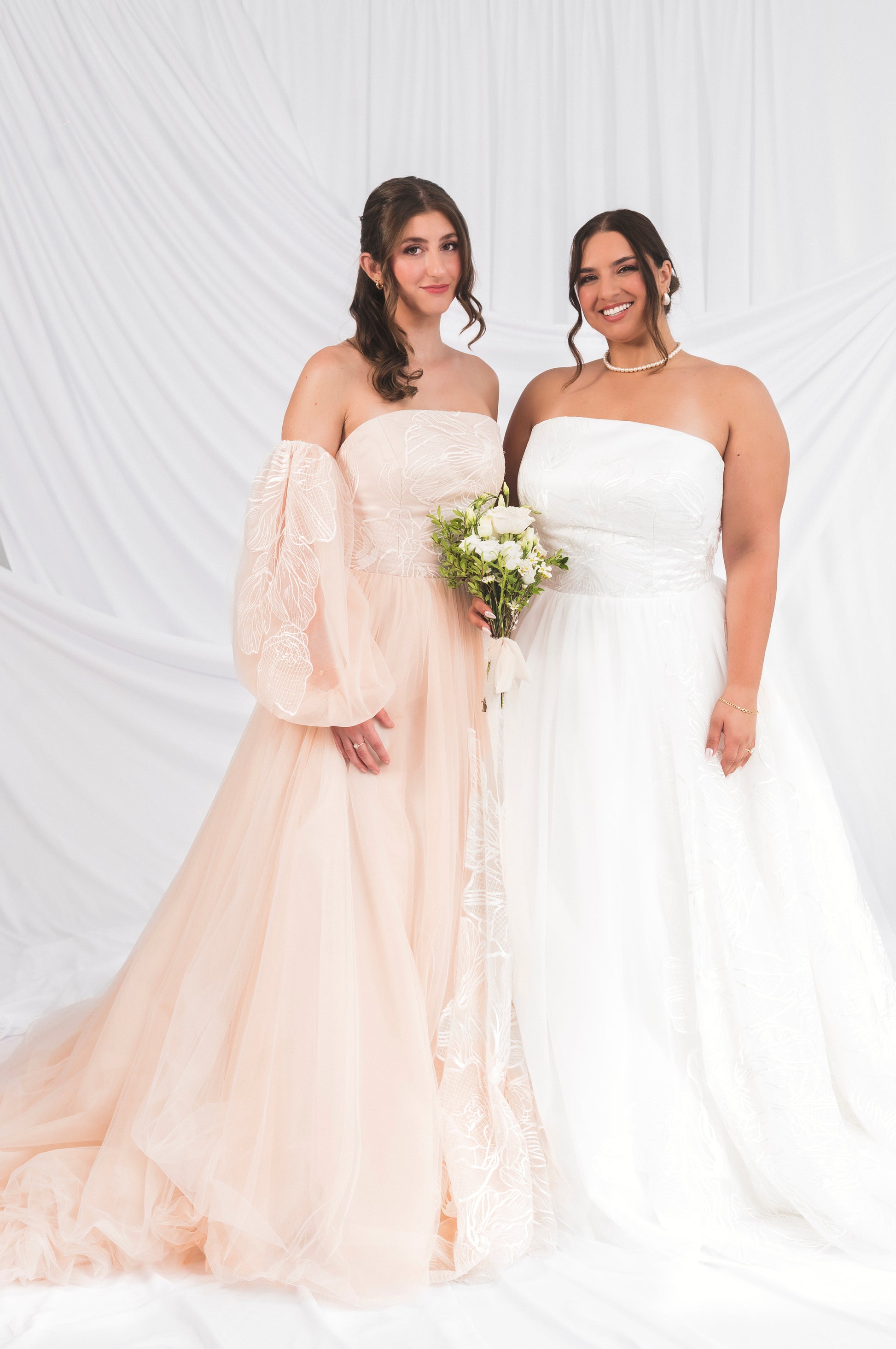 bride wearing blush ball gown gown with ballon sleeves and floral embroidery with a dramatic long train beside a plus size bride wearing a silk white tulle ballgown briar with large floral embroidery with a long train. 