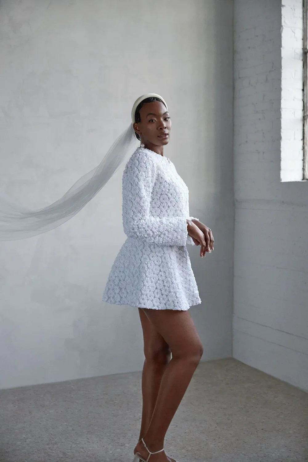 Side view of a Bride against a neutral background wearing a matching little white dress in ottawa. A cropped jacket and flared mini skirt.