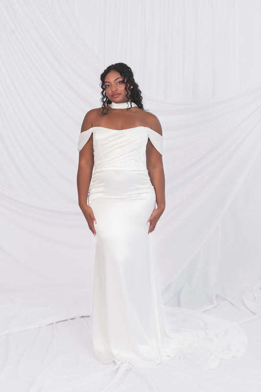 Woman wearing a white off-shoulder gown against a white background in Ottawa. Draped bodice and swag sleeves, satin simple bridal scarf and long train