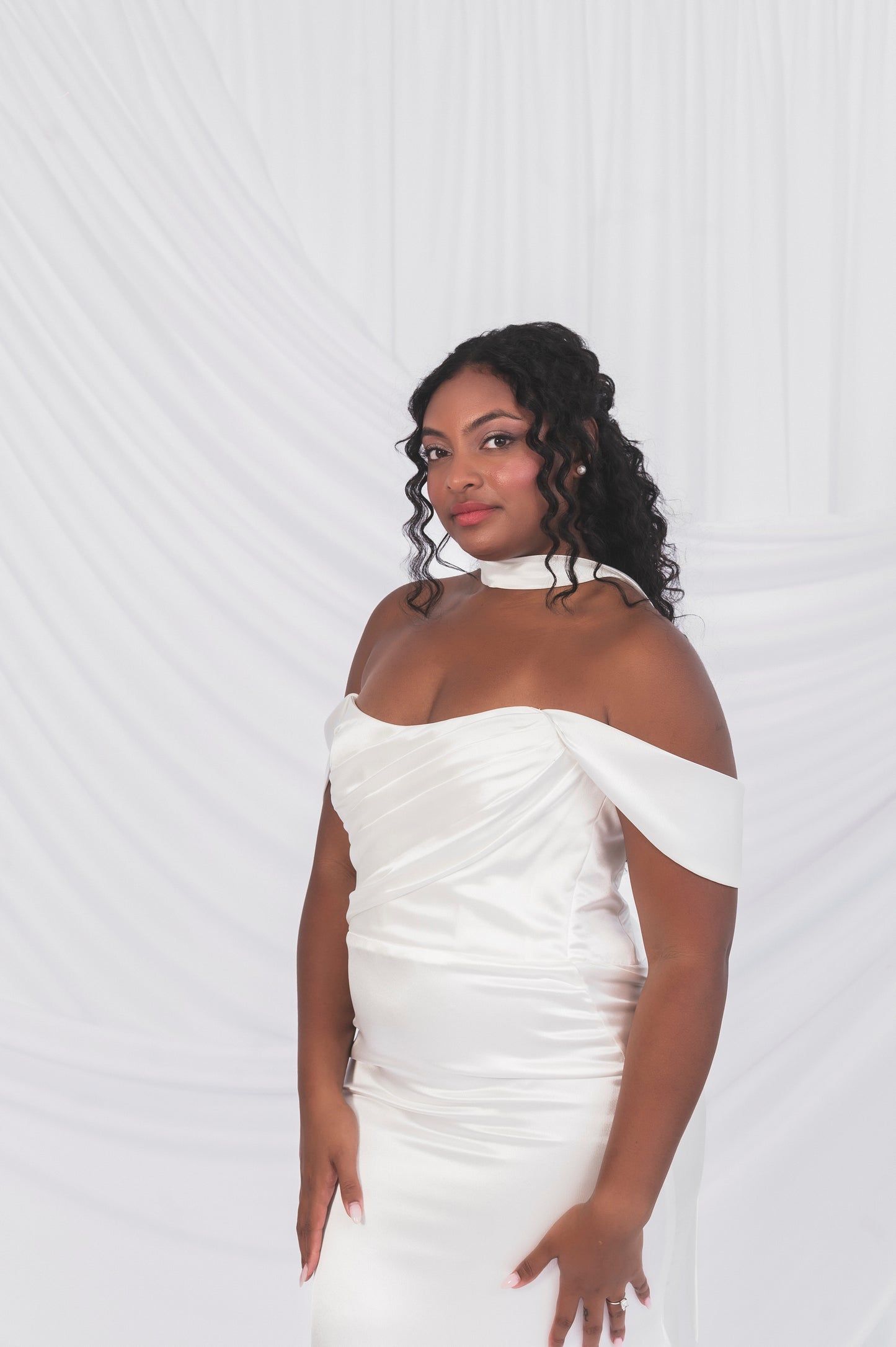 Woman wearing a white off-shoulder gown against a white background in Ottawa. Draped bodice and swag sleeves, satin simple bridal scarf 