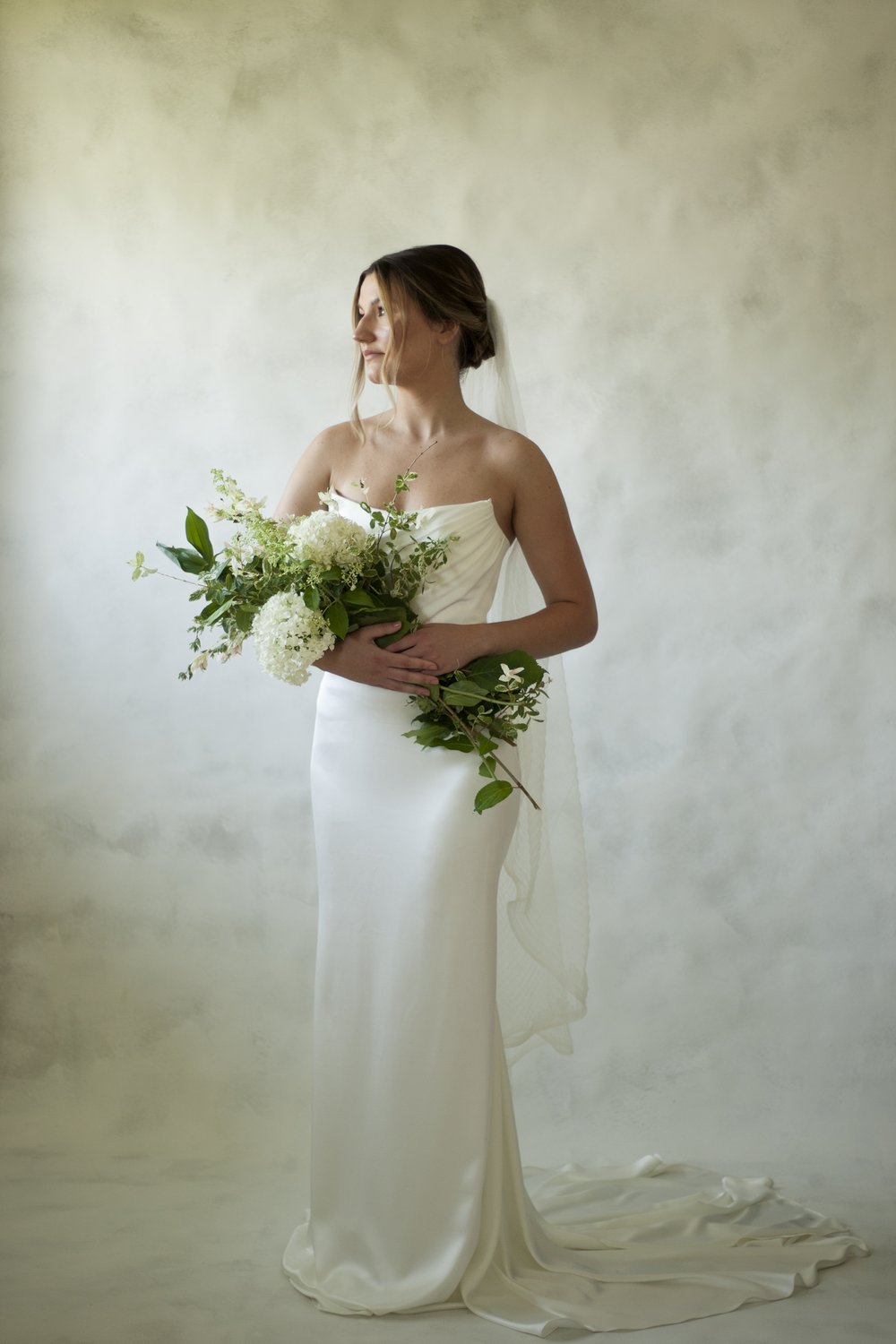A texture satin crepe gown featuring movement in a fit and flare profile with a delicate draped bodice