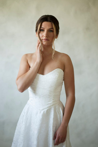 Meet Klein, stunning with a floral jacquard fabric and delicate full skirt. A soft scooped neckline and angular draped bodice create the beauty of Klein.