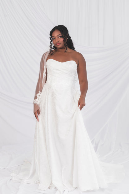  A black bride wearing a white strapless gown with floral details, jacquard print, with a matching veil  against a white background in Ottawa Canada.