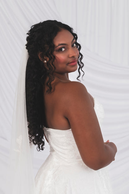 Woman in a white dress with long, styled hair against a white background