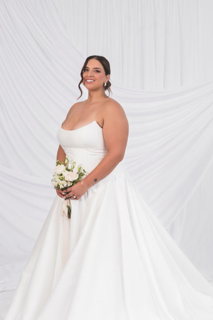 Side view of the tear drop waisted gowns, plus size bride holding a bouquet with a cat eye neckline and big train