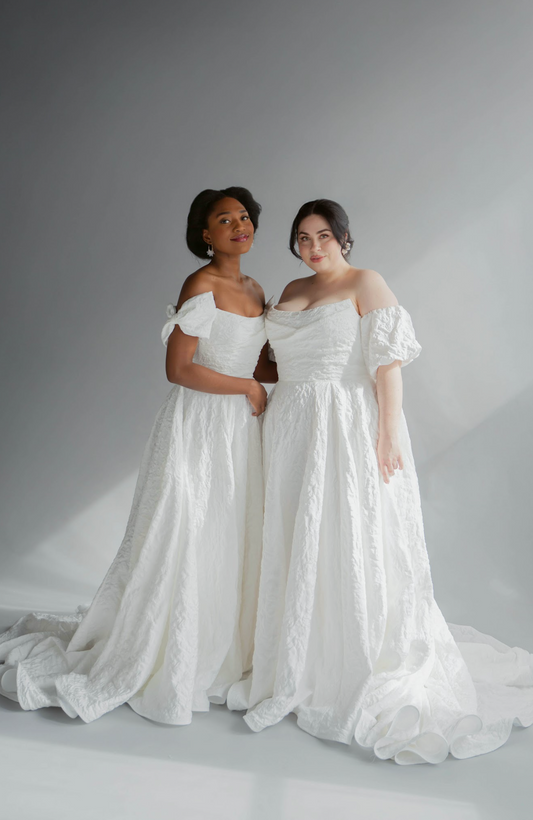 Two women wearing the cat eye puffy jacquard Aline Gown, auren. One is shown in a plus size with a puff off the shoulder