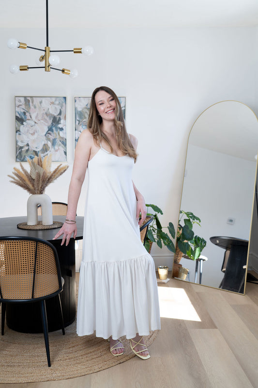 Woman in a white dress standing in a modern interior setting with a mirror and decor.