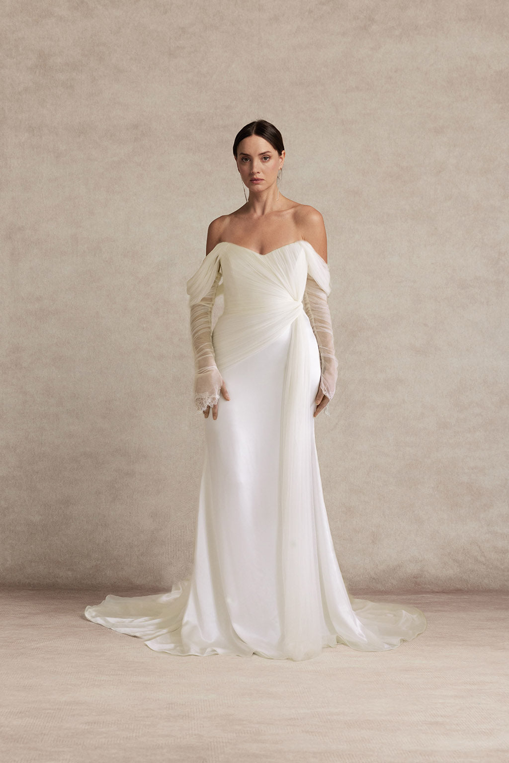 Woman wearing a white off-shoulder gown with sheer sleeves against a beige background | Ouma Elysian Dress 