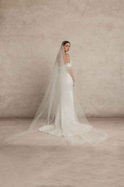 Bride in a white wedding dress, Elysian by Ouma, featuring the off the shoulder soft sweatheart neckline and fitted satin silk bodice. Pearl buttons cascading down the back bodice and a modest cathedral length train.  Matching veil at extra royal cathedral length