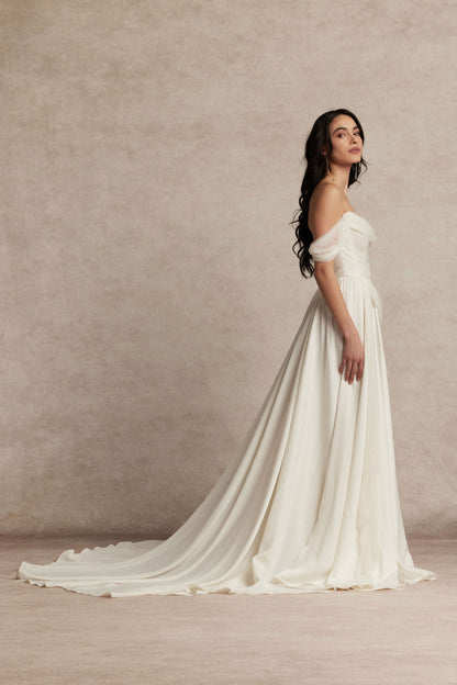 Woman in a white wedding dress against a beige background, silk tulle the Sora dress by Ouma