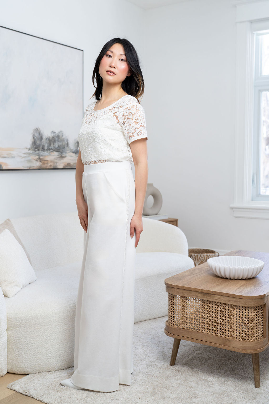 Woman in a white lace dress standing in a bright living room.